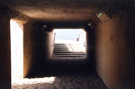 Excerpt From Chasing The Dime (Photo by Wendy Werris)
Pierce took the California Incline down to the coast highway and then north to the mouth of Santa Monica Canyon. He turned right on Channel and parked at the first meter he found open. He then got out of the BMW and walked back toward the beach, looking over his shoulder and about him every ten yards for followers. When he got to the corner he looked around once more and then quickly went down the stairs into the pedestrian tunnel that went under the highway to the beach.
The walls of the tunnel were a collage of graffiti, some of it recognized by Pierce even though it had been at least a year since he had walked through the tunnel. During happier times with Nicole it had been their routine to get the paper and coffee on Sunday mornings and take it all down to the beach. But in the last year Pierce was working on Proteus most Sundays and didn't have time for the beach.
On the other side the tunnel branched into two separate staircases leading up. He knew the further staircase came up on the sand right next to the drainage channel that emptied surface water runoff from the canyon into the ocean. He chose this stairway and came up into the sunlight to find the beach deserted. He saw the yellow lifeguard stand where he and Nicole would have their coffee and read the paper. It looked as abandoned as their Sunday ritual had become. He just wanted to see it, to remember it, before he went up the hill to her. After a while he turned back to the mouth of the tunnel and went back down the stairs.
A quarter way back through the sixty yard tunnel Pierce saw a man coming down the opposite staircase. Because of the light from above him, the man was in silhouette. Pierce was suddenly stricken with the thought of a confrontation with Renner in the tunnel. The cop had followed him and was here to arrest him. Santa Monica Beach Tunnel