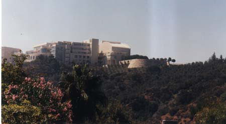 Excerpt From A Darkness More Than Night (Photo by Wendy Werris)
As the freeway rose to cross the Santa Monica mountains in the Sepulveda pass, McCaleb saw the Getty rise in front of him on the hilltop. The structure of the museum itself was as impressive as any of the great artworks housed within. It looked like a castle sitting atop a medieval hill. He saw one of the double-trams slowly working its way up the side of the hill, delivering another group to the altar of history and art. The Getty Museum