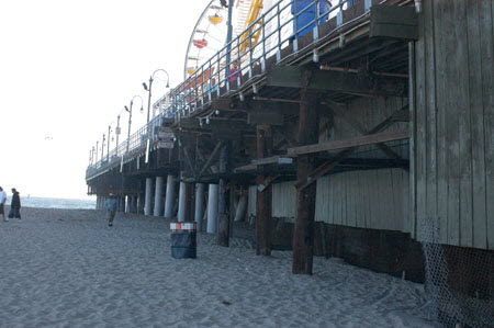 Excerpt from The Reversal (photo credit: Wendy Werris)
Bosch put the phone away and headed toward the pier. The wind was strong off the water and a fine mist of sand stung his face and eyes as he approached the huge structure. The pier was like a beached aircraft carrier. It was long and wide. It had a large parking lot and an assortment of restaurants and souvenir shops on top. At its midpoint it had a full amusement park with a rollercoaster and the signature Ferris wheel. And at its furthest extension into the sea it was a traditional fishing pier with a bait shop, management office and yet another restaurant. All of it supported on a thick forest of wood pilings that started landside and carried 700 feet out beyond the wave break and to the cold depths.
Landside, the pilings were enclosed with a wooden siding that created a semi-secure storage facility for the city of Santa Monica. Only semi-secure for two reasons: The storage area was vulnerable to extreme high tides which came on rare occasion during offshore earthquakes. The pier also spanned a hundred yards of beach, which entailed anchoring the wood siding in moist sand. The wood was always in the process of rotting and was easily compromised. The result was that the storage facility had become an unofficial homeless shelter that had to be periodically cleared out by the city. Underneath the Santa Monica Pier